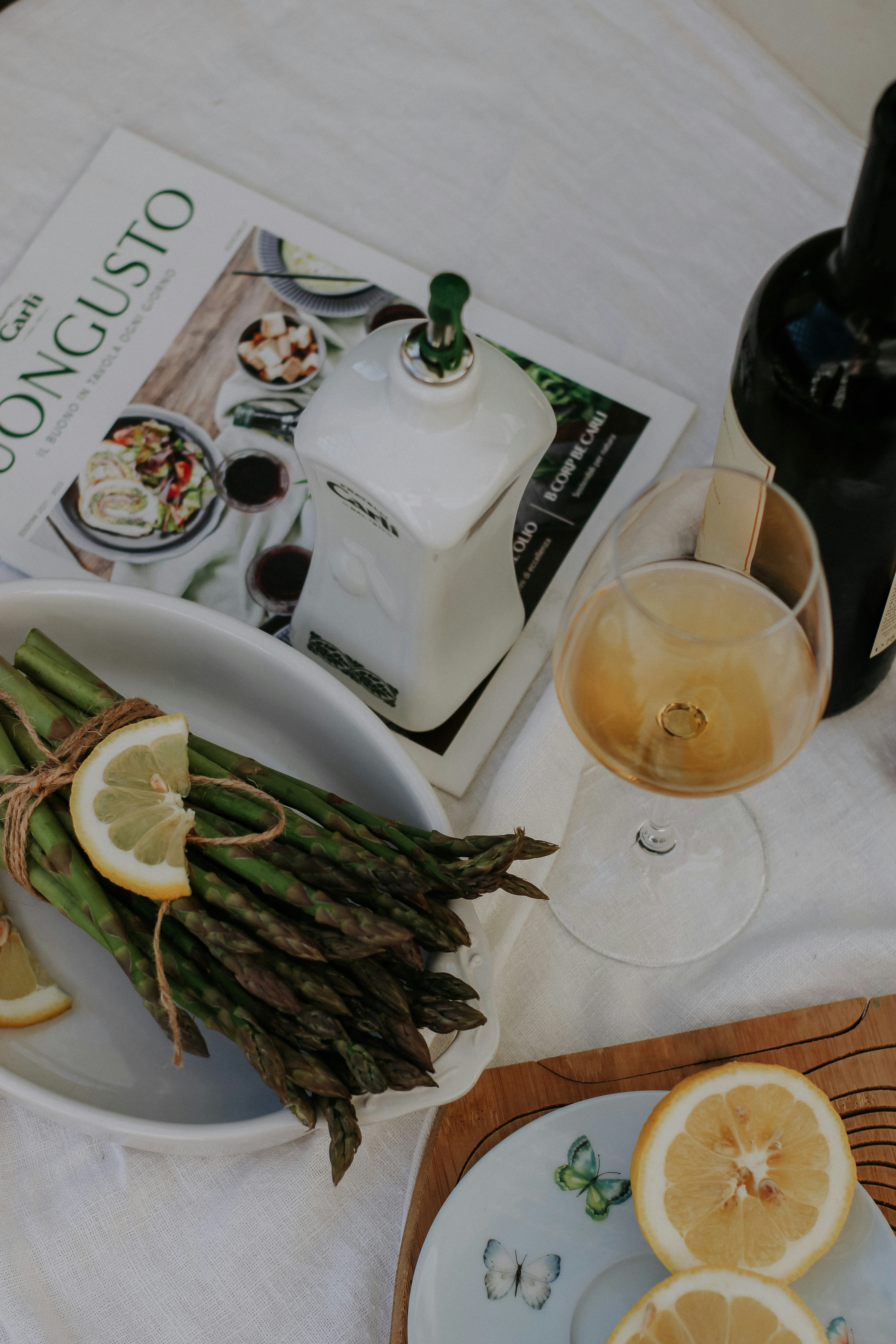 a lovely white table with aspargus, a magzine, a glass of wine to unwind and enjoy the ritual of light elegant dinners